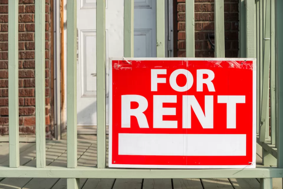 Close-up of red For Rent sign with white text on porck of brick building.